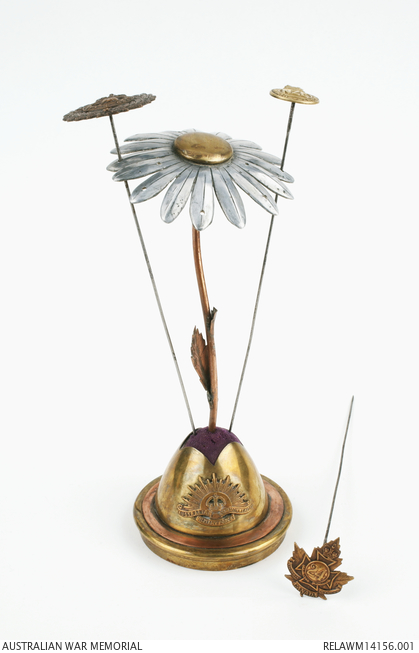 Making jewellery in a time of war:
Set of hat pins and field daisy shaped stand . Made from the nose cone of a shell, bicycle spokes, uniform buttons and shell fragments by Stanley K Pearl, 1918. Australia War Memorial collection 