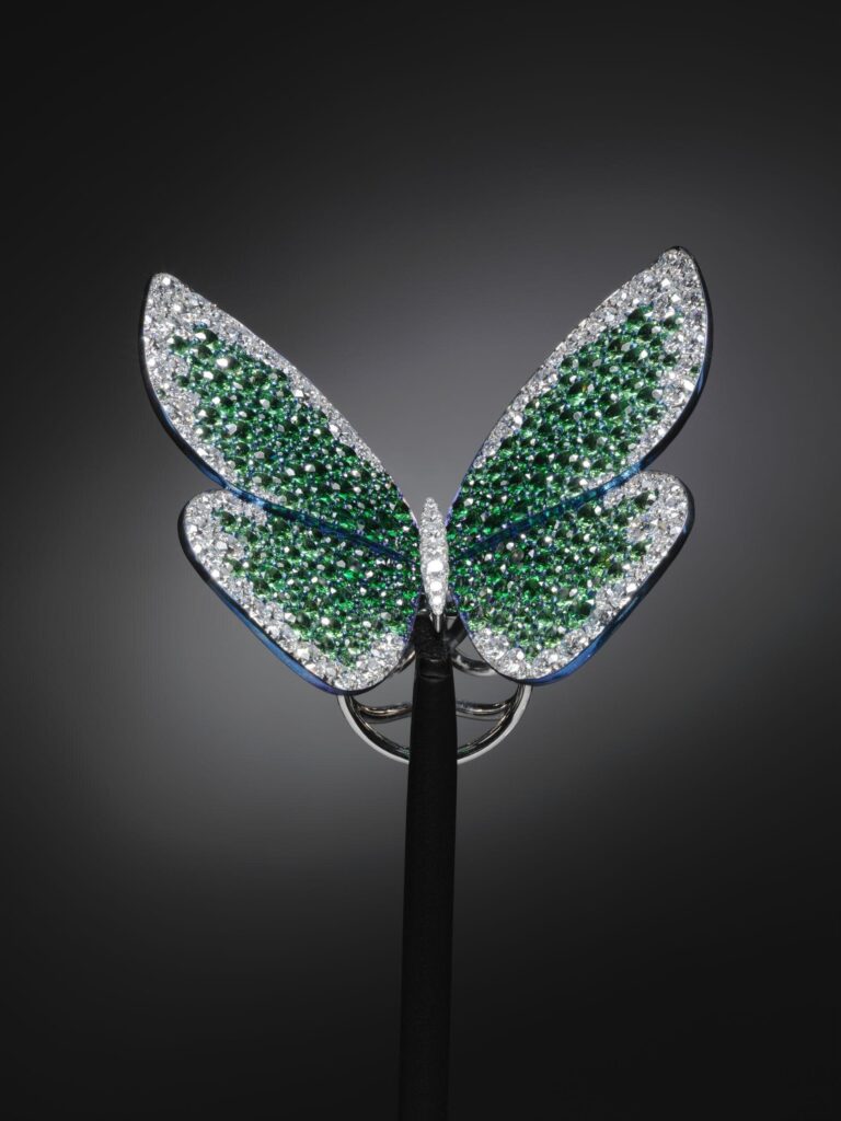 Ring in the form of a butterfly. A pair of blue titanium wings, each in two sections, set with tsavorites and diamonds. The wings are joined by a hinge underneath the insect's diamond-set, white gold body. The band is an intricate, curving, hinged structure of white gold set with diamonds, which enables the wings to move as the wearer's finger bends.