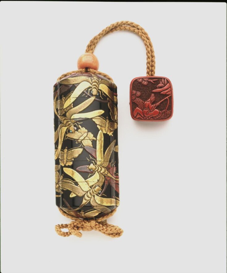 Inro depicting dragonflies and butterflies in gold, red and silver takamakie lacquer on a black ground. Formed as a  cylinder wtih rounded ends and dividing into three sections. The sections are joined by a yellow plaited cord with a bead at the top and a carved counterweight. 