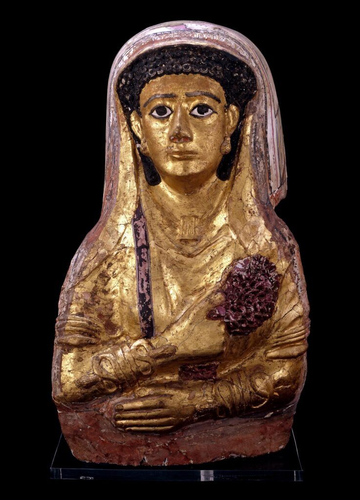 Mummy portrait showing a half length young woman with black hair. She is wearing a veil and holds a bunch of flowers. Two large snake bracelets cover each of her lower arms. 