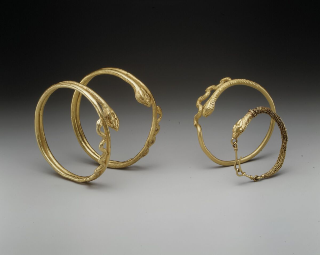 Group of four gold Roman snake bangles showing the loops of the tail and large snake heads. 