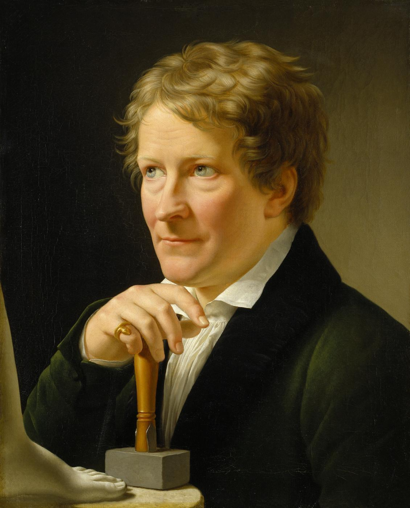 Half length portrait of Danish sculptor Bertel Thorvaldsen, wearing a dark jacket over a pleated white shirt and open collar. He is shown looking to the left and with his hand on a mallet. The foot of a marble statue on a plinth appears in the left hand corner of the painting. A gold snake ring is on the little finger of his right hand. 