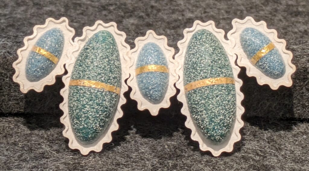 Blue brooch by Liu Qiwei with five oval shapes with a gold band horizontally place across each and a white frame with pie crust edging. 