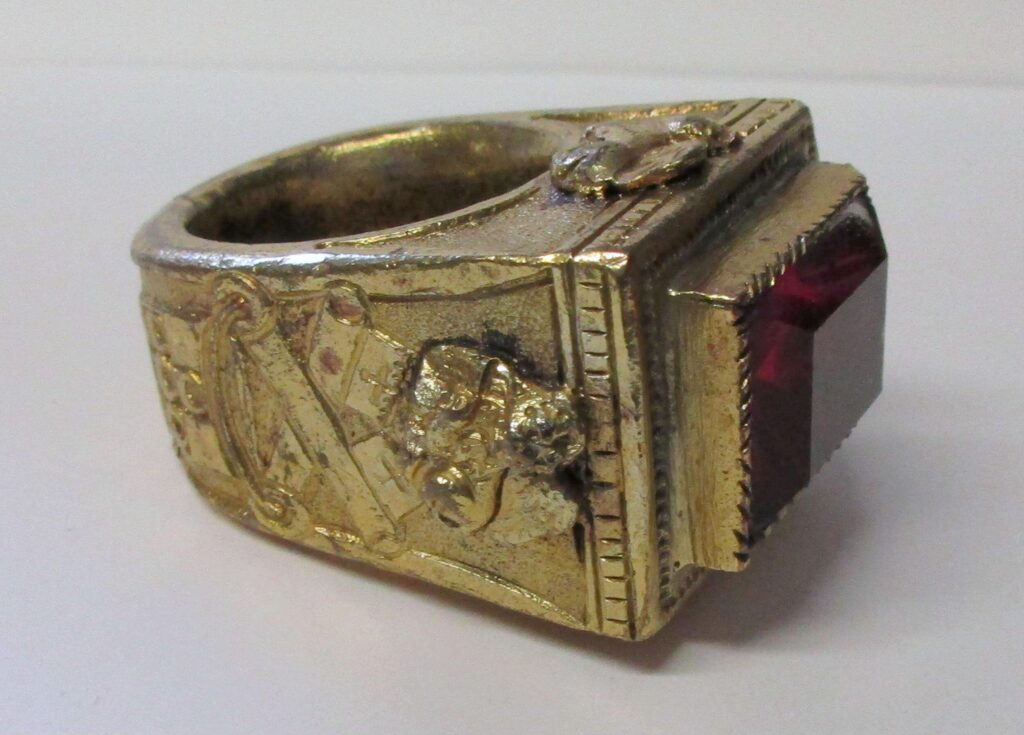 Gilt copper ring with red glass stone. Cast with papal arms on the shoulders. Part of Edmund Waterton's ring collection.