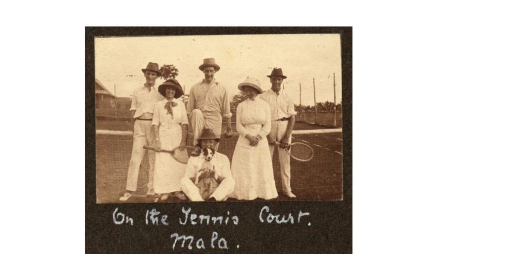 Sepia photograph of a group of tennis players. Three men in hats and white trousers and shirts stand at the back, then two women in long white dresses and sun hats. The centre of the picture is a seated man with a small dog on his knees. The inscription 'on the Tennis court. Mala.' is handwritten under the image.