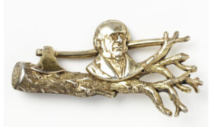 Silver gilt brooch of busy Prime Minister William Gladstone above a cut tree with an axe horizontally behind. Birmingham 1898-9