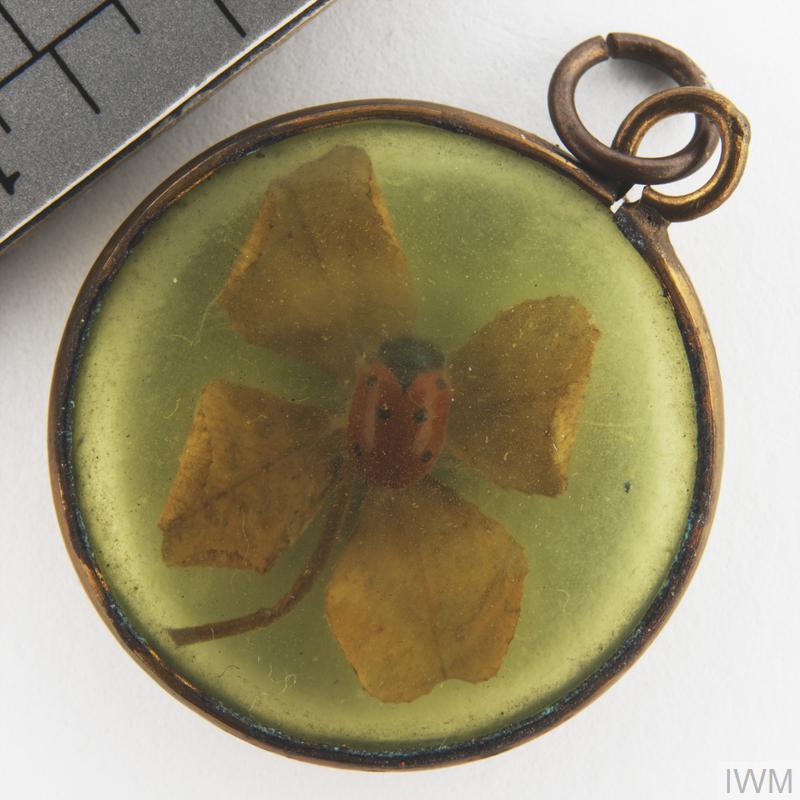 Yellow metal circular locket with glass window showing a four leaf clover and a ladybird. Lucky token from World War 1, Imperial War Museum. 