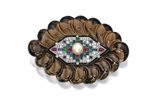 Eye shaped brooch with an outer border formed from scales of smokey brown quartz. The centre is a navette shaped metal framework set with a mosaic of diamonds, rubies, emeralds and sapphires, like an embroidery pattern. A pearl is set in the centre. 