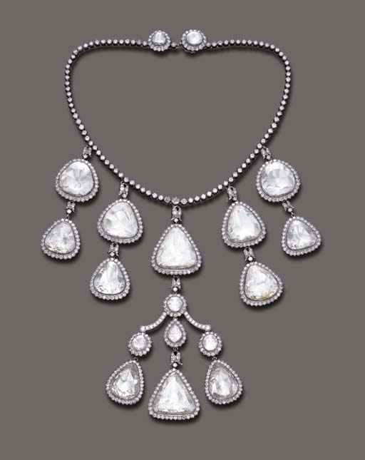 Necklace made up of a circlet of small diamonds from which are suspended a central ornament like a chandelier style earring formed of a flat diamond set over a silver backplate. This central motif has a two pendants made up of two diamonds set in silver placed one above the other on each side of the necklace. 