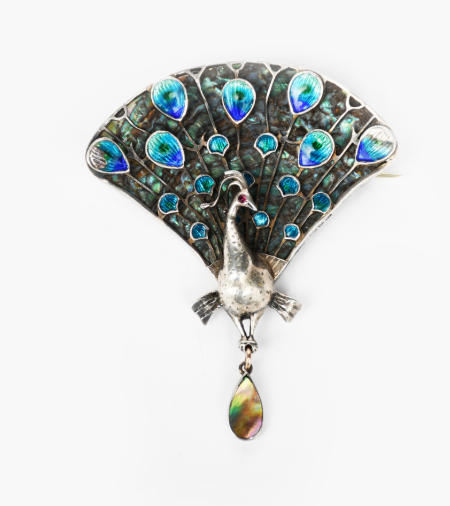 A fine Guild of Handicraft silver and enamel peacock brooch designed by Charles Robert Ashbee, wirework feathers with enamelled blue and green eyes, set on mother of pearl shell back, the bird set with demantoid garnet eye, holding a mother of pearl drop, stamped marks to side and back, GofH Ltd mark, London 1907, 7.5cm. high