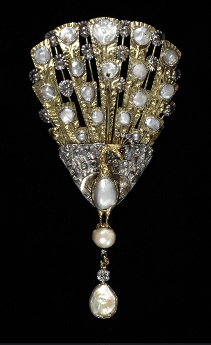 Gold, silver , blister pearl, garnet and brilliant cut diamond brooch in the shape of a peacock facing forwards. The tail is chased with feather decorations and set with circular blister pearls set in silver. The brooch has a long pendant with two pearls separated by a diamond. 